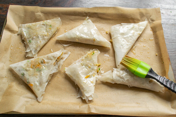 Preparing Samsa for Baking Uncooked samsa pastries on a baking sheet and being brushed with oil before baking.