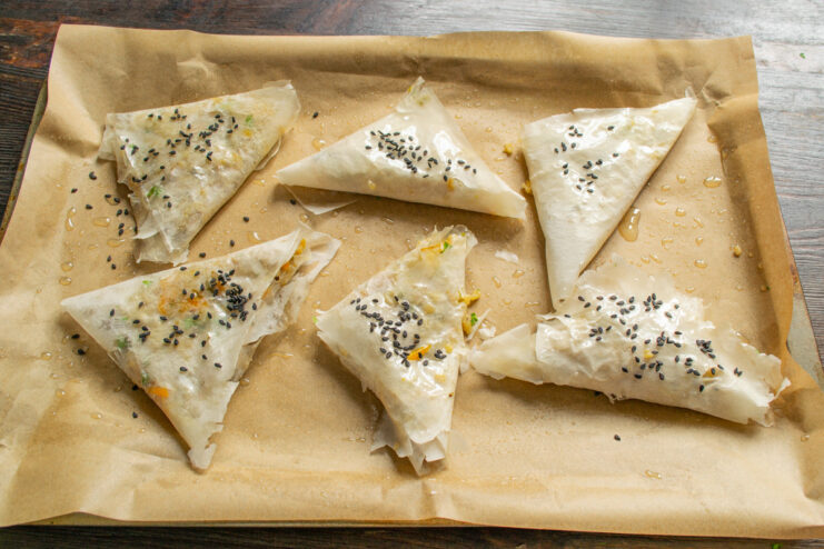 Garnishing Samsa with Sesame Seeds Before Baking Samsa pastries on a baking sheet being sprinkled with sesame seeds before going into the oven.