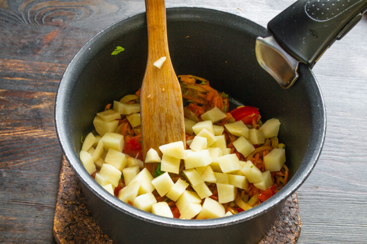 Adding potatoes to make the soup more substantial Diced potatoes being added to the pot with other vegetables.