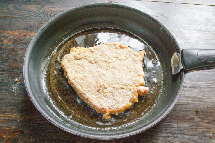 Frying the Schnitzel to a Golden Brown A pork schnitzel frying in a pan, turning golden brown on one side.