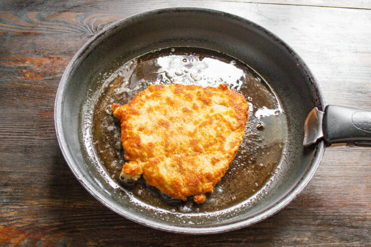 Cooking Both Sides of the Schnitzel Until Crispy Flipping a pork schnitzel in a hot pan to cook the other side.