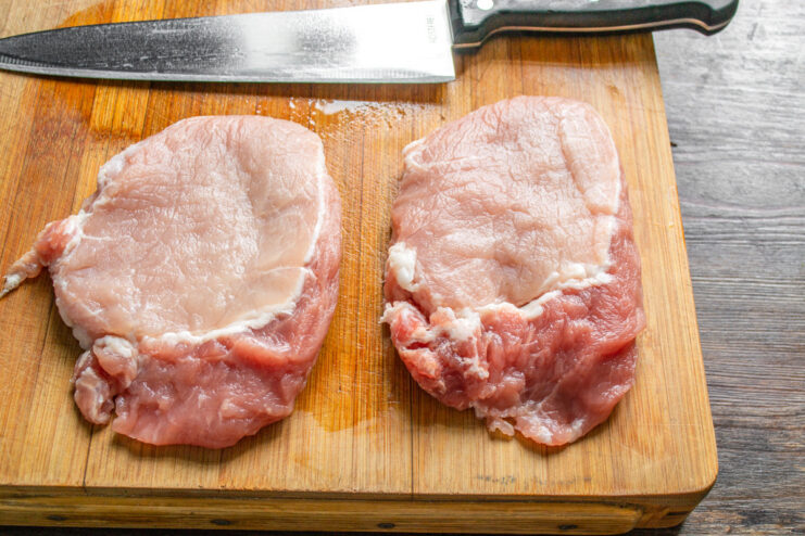 Preparing Pork Loin for Schnitzel Two thick slices of raw pork loin on a cutting board, ready to be prepared for schnitzel.