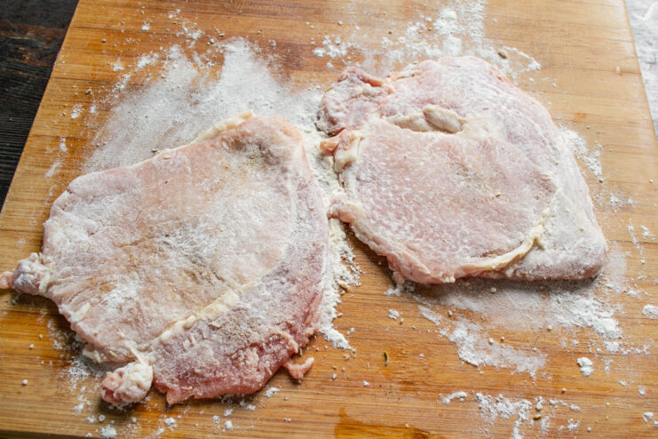 Dredging Schnitzel in Flour - First Breading Step Coating a seasoned pork cutlet in flour as the first step of breading.