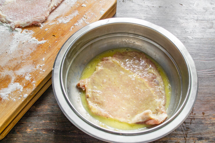 Coating the Schnitzel in Egg Wash Dipping a flour-coated pork cutlet into a bowl of whisked egg.