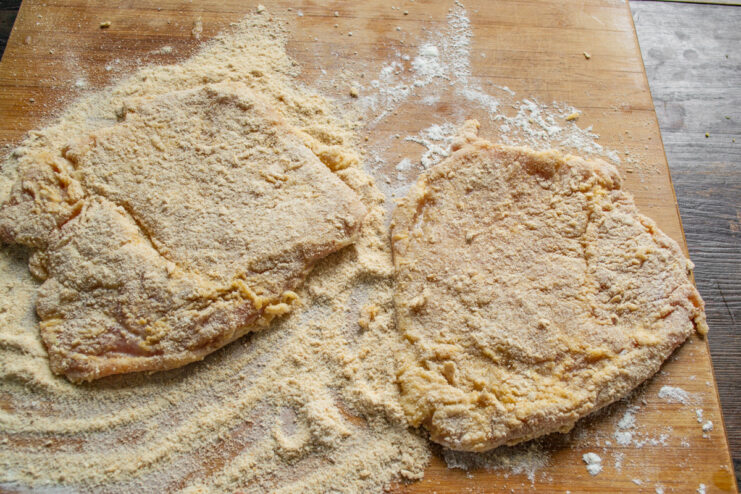 Breading the Schnitzel with Breadcrumbs Coating an egg-washed pork cutlet in a layer of breadcrumbs on a board.