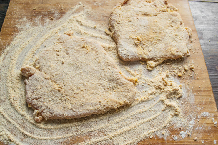 Preparing Schnitzel Ahead of Time Two fully breaded raw pork schnitzels on a plate, ready for cooking or refrigeration.