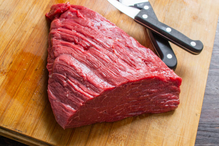 Preparing the Beef: Trimming the Silverskin from the Tenderloin A hand with a knife trimming the silverskin off a raw beef tenderloin on a cutting board.