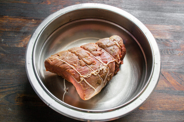 Cooling the Cooked Ham in an Ice Bath The cooked beef ham, still in its bag, is placed in a bowl of cold water to cool down.