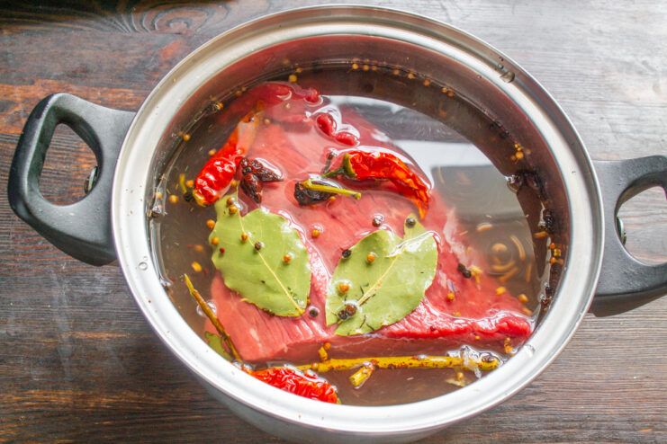 Marinating the Beef: Submerging the Tenderloin in the Cooled Brine A piece of beef tenderloin being placed into a pot of cooled, spiced marinade.