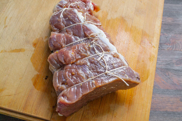Bagging the Beef: Sealing the Meat for Cooking A marinated and tied piece of beef being placed into a clear ziplock bag.