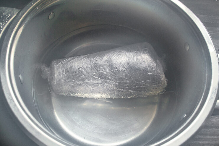 Maintaining the Perfect Cooking Temperature with a Thermometer A zip-lock bag with seasoned beef submerged in a pot of hot water with a thermometer showing the temperature.