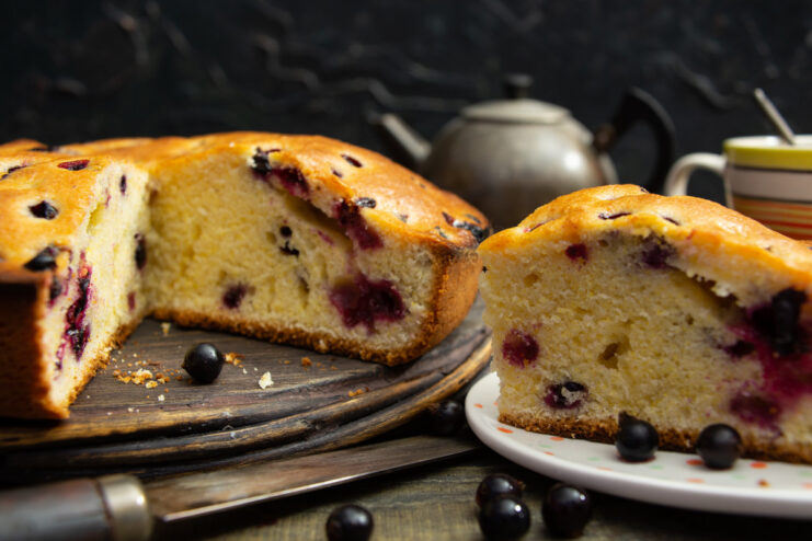 A slice of fluffy blackcurrant milk cake, dotted with berries, served on a white plate.