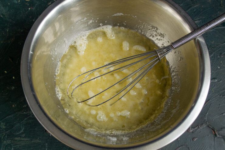 Step 2: Adding melted butter to the egg mixture Pouring a stream of melted butter from a small bowl into the egg and sugar mixture.
