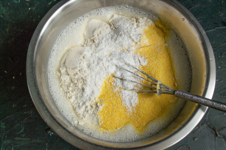 Step 5: Adding dry ingredients to the batter Adding a mix of all-purpose flour, corn flour, and baking powder to the wet ingredients in a bowl.