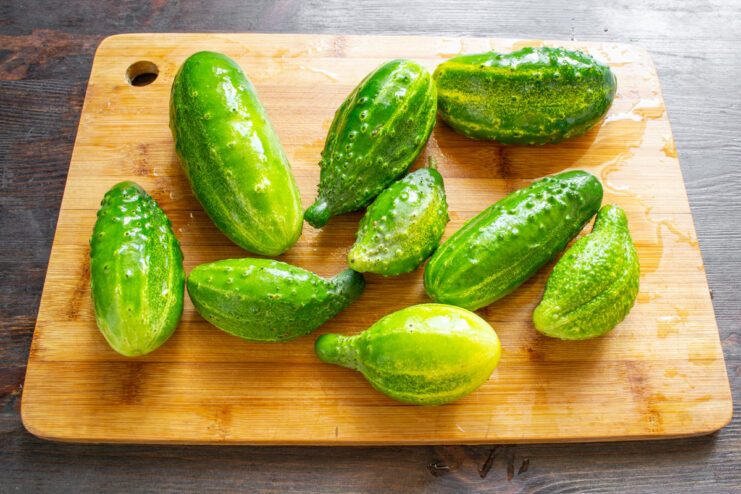 Washing the Cucumbers Before Preparation A pile of large, overgrown cucumbers in a metal bowl being washed with water.