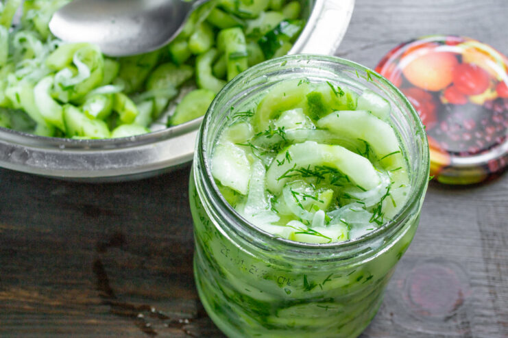 Topping Off the Jars with the Released Juice Pouring the juice from the marinating bowl into a jar filled with cucumber salad.