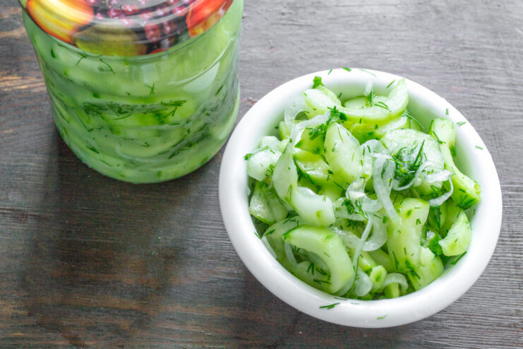 The Color Change of Cucumbers After Sterilization A bowl of leftover green cucumber salad next to sealed jars where the cucumbers have turned a brownish, cooked color.