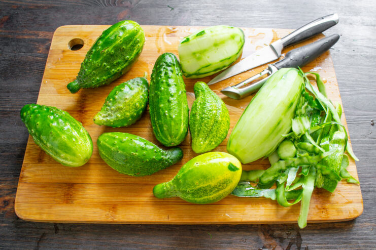 Peeling the Tough Skin from the Overgrown Cucumbers A hand using a vegetable peeler to remove the tough, yellowed skin from an overgrown cucumber.