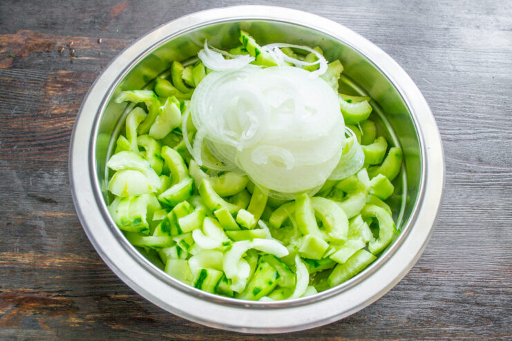 Adding Thinly Sliced Onions to the Cucumbers A bowl of sliced cucumbers with thinly sliced onion rings being added on top.