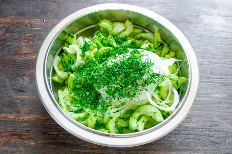 Adding Freshly Chopped Dill for Flavor A bowl of sliced cucumbers and onions with a generous amount of freshly chopped dill added.