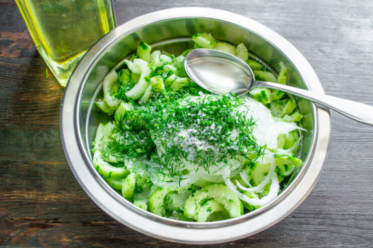 Seasoning the Vegetable Mixture A bowl of cucumber salad with salt, sugar, vinegar, and oil being added.