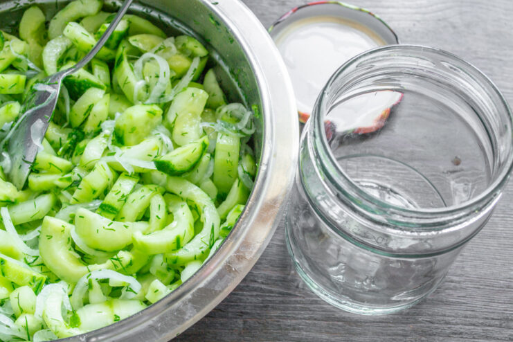 Packing the Salad into Sterilized Jars A person packing the prepared cucumber salad tightly into a clean glass jar.