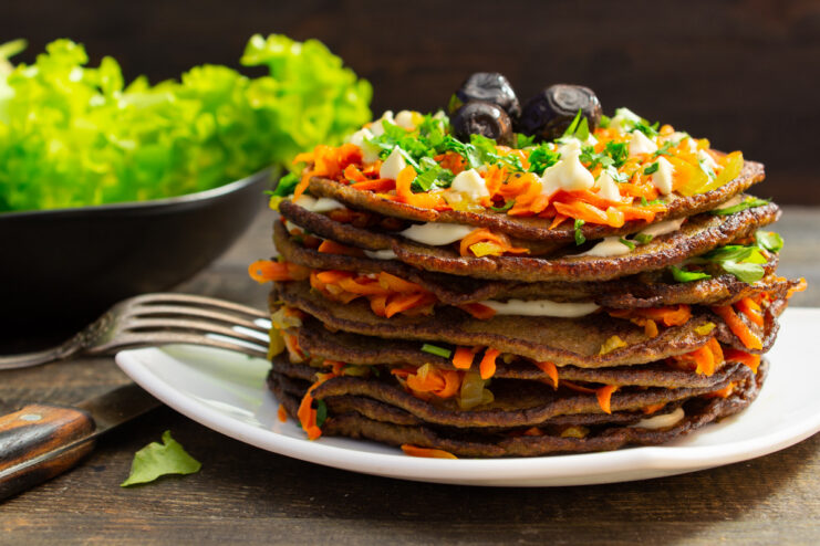 A finished savory beef liver cake on a plate, garnished with mayonnaise, herbs, and olives.