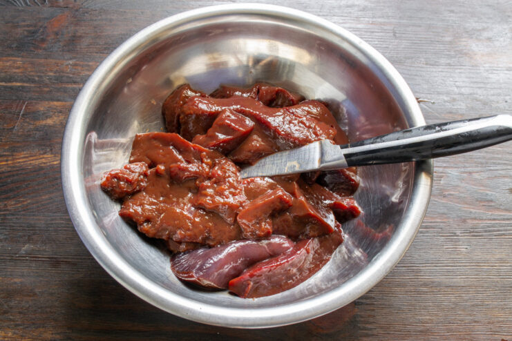 Preparing the beef liver by cutting it into small, manageable pieces Pieces of raw beef liver in a white bowl, ready for the next step.