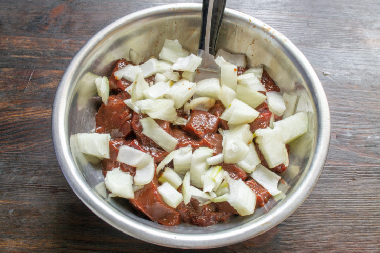 Adding finely chopped onion to the beef liver for the batter Finely chopped onion being added to a bowl of raw beef liver pieces.
