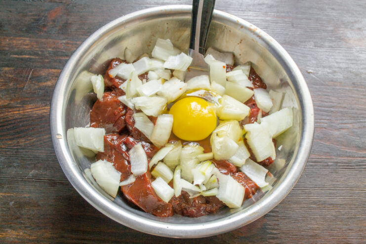 Adding an egg to the liver and onion mixture A raw egg cracked into a bowl containing beef liver and chopped onion.
