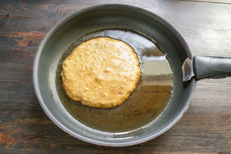 Frying a thin liver pancake in a hot skillet A thin, round liver pancake cooking in a black frying pan.