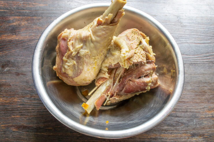 Removing the tender, cooked turkey from the flavorful broth. Cooked turkey drumsticks being lifted out of a pot of broth with a slotted spoon.
