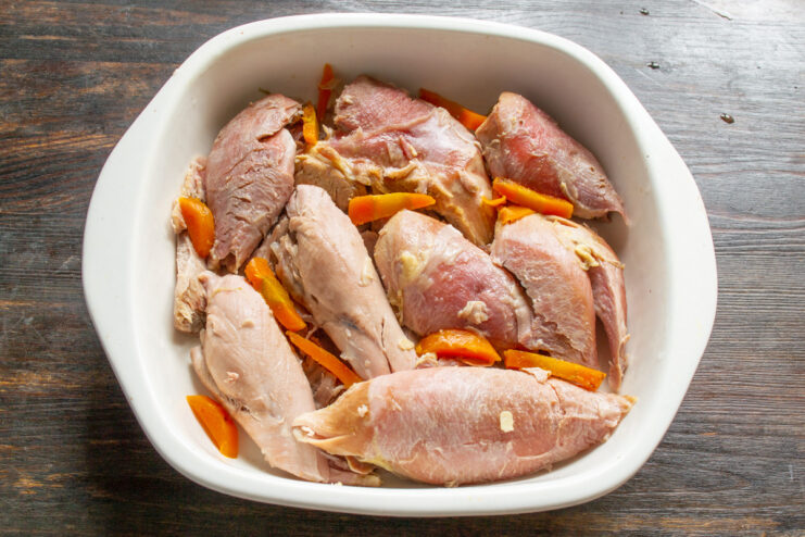 Arranging the turkey and carrots to create a beautiful mosaic in the aspic. Pieces of cooked turkey and bright orange carrot slices arranged neatly in a shallow glass dish.