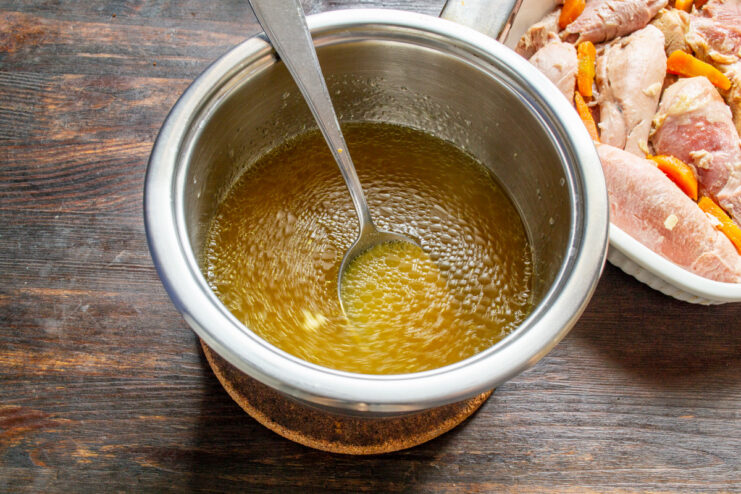 Gently heating the broth to ensure the gelatin dissolves completely without boiling. A pot of broth with gelatin being heated gently on a stove, with steam rising.