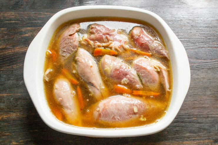 Pouring the savory broth over the turkey to create the aspic. Pouring the warm gelatin-infused broth over the arranged turkey and carrots in a glass dish.