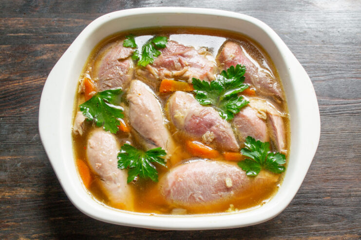 Adding a fresh touch with parsley before chilling the aspic. Placing fresh parsley leaves on top of the turkey and broth in a dish before it sets.