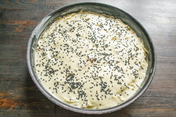 Sprinkling the top of the pie with sesame seeds for extra flavor and a beautiful crust. Sprinkling black sesame seeds on top of the uncooked batter pie in a baking pan.