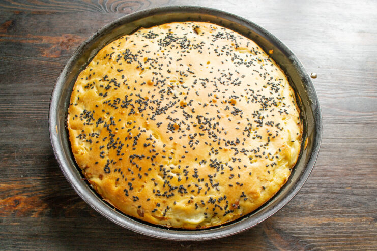 Placing the pie in a preheated oven to bake until golden brown and cooked through. Placing the baking pan with the pie into a hot oven.