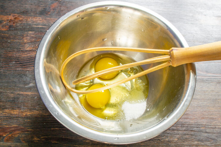 Preparing the batter base: combining eggs, salt, and sugar in a bowl before whisking. A glass bowl containing two cracked eggs, with salt and sugar added.