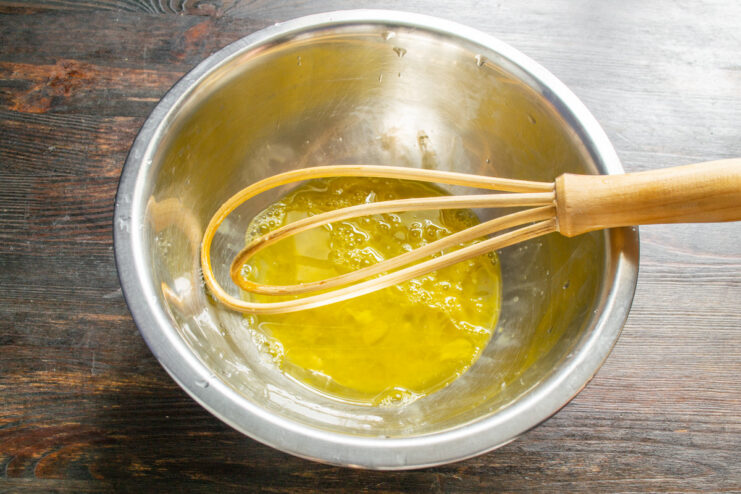 Whisking the eggs until just combined. No need to beat them into a foam for this batter. A hand using a whisk to mix eggs in a glass bowl.