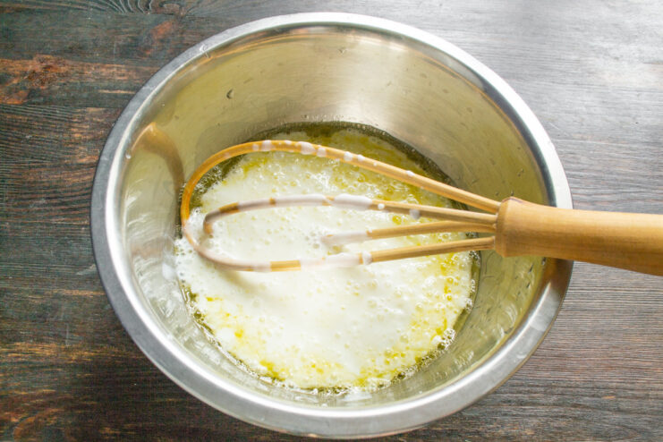 Adding kefir to the egg mixture. Kefir will make the batter tender and moist. Pouring kefir from a carton into a glass bowl with whisked eggs.