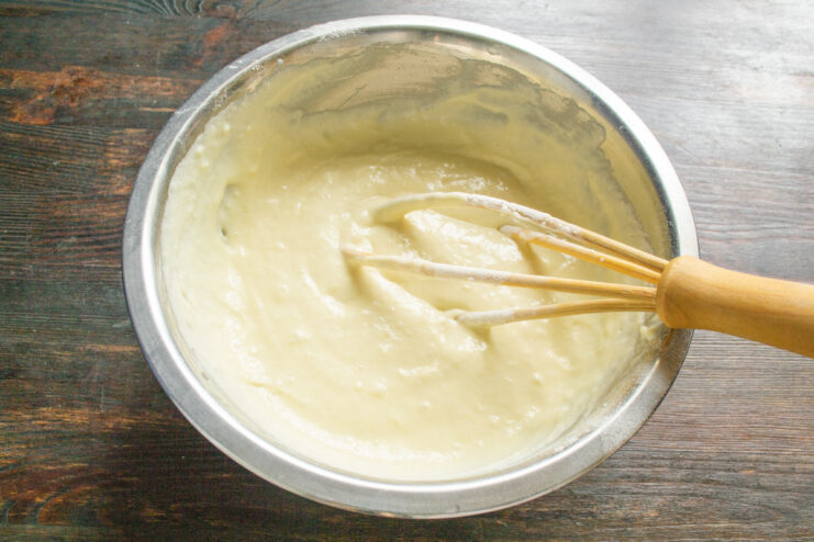Mixing the batter with a whisk until it's smooth and uniform. A hand mixing the pie batter in a glass bowl with a metal whisk.