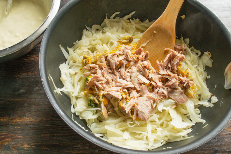 Combining the stewed cabbage with tushonka to create the savory pie filling. Mixing stewed cabbage and tushonka (canned stewed meat) in a skillet for the pie filling.