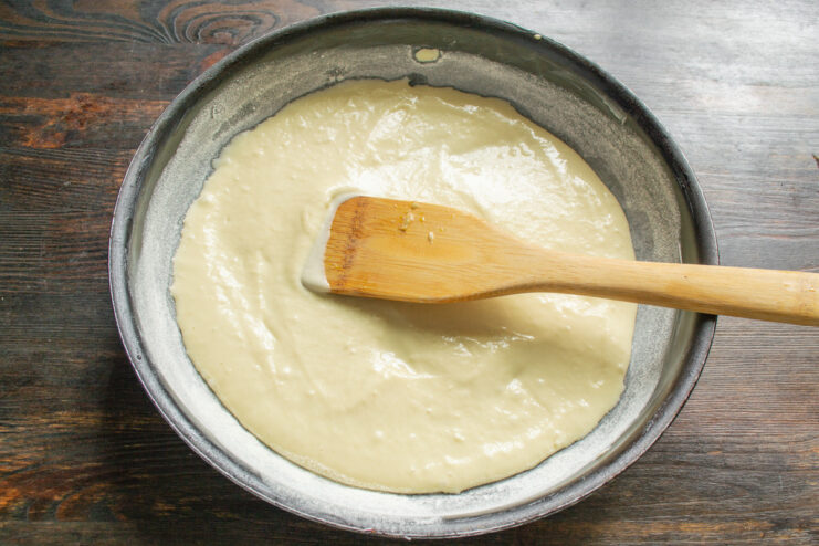 Pouring the first layer of batter into the greased and floured baking pan. Pouring half of the pie batter into a round, greased baking pan.
