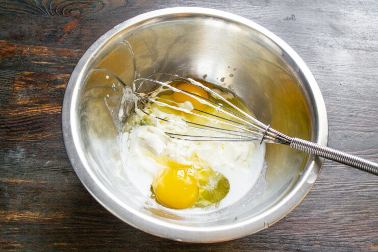 Step 1: Cracking eggs into the wet ingredients Cracking eggs into a bowl with mayonnaise and sour cream.