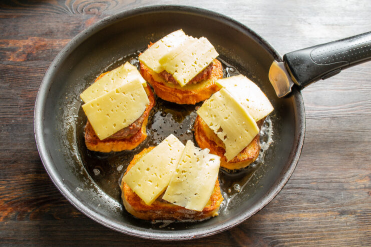 Topping with Generous Slices of Cheese Slices of hard cheese being placed on top of the beef patties in the pan.