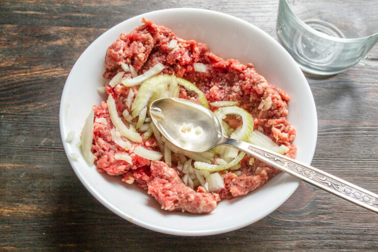 Adding Onion and Water for Juiciness Adding finely chopped onion and cold water to the ground beef in a bowl.