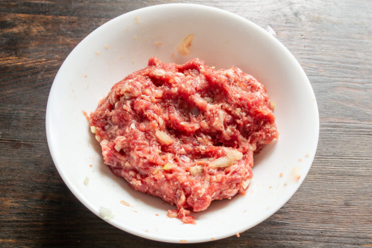 Flavoring the Meat with Your Favorite Spices Sprinkling ground meat seasoning into the bowl with beef and onions.