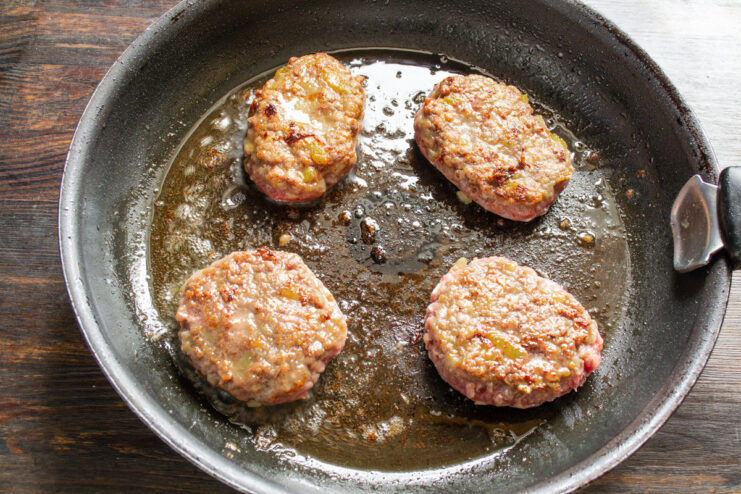 Quickly Searing the Patties to Lock in Juices Beef patties being pan-fried in a skillet until golden brown on one side.