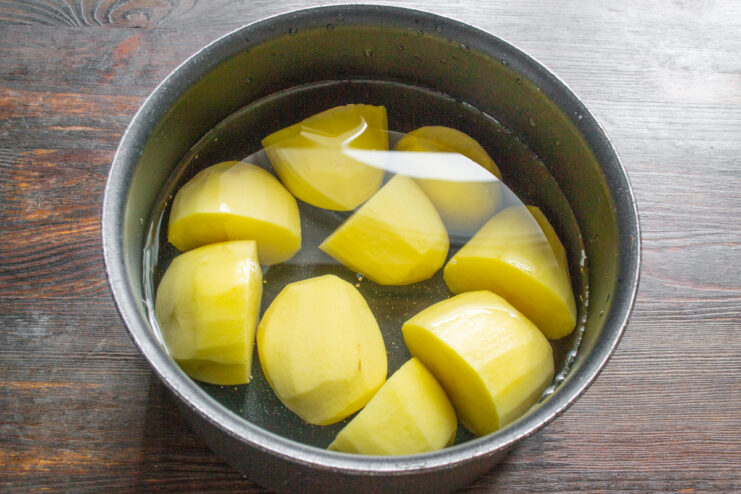 Peeled potatoes boiling in a pot of water on the stove.